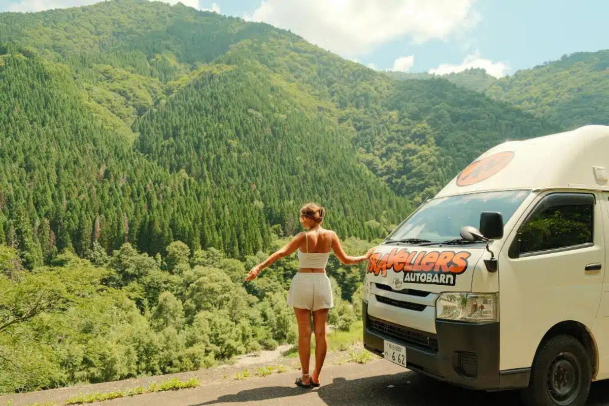日本の山々を背景にTravellers Autobarnのキャンピングカーで冒険を楽しむ女性