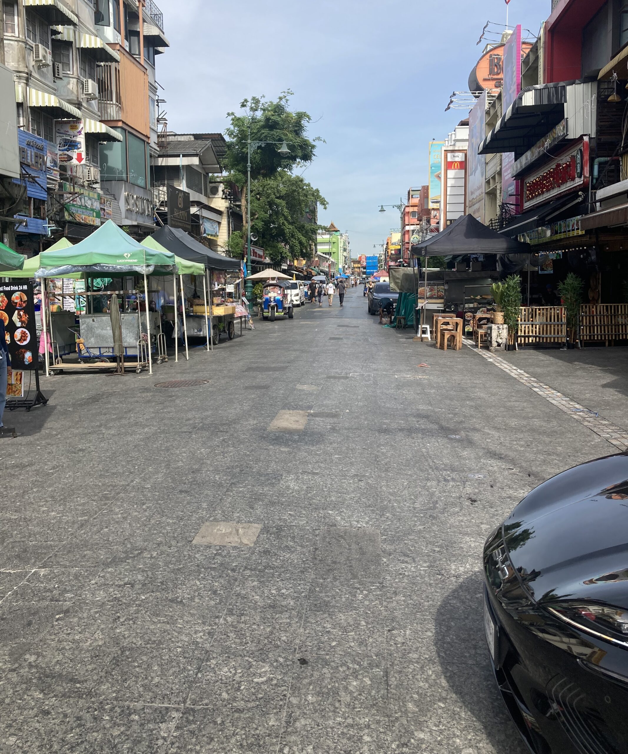 朝のカオサンロード。屋台のテントが並び、トゥクトゥクや街路樹が見える静かな通り